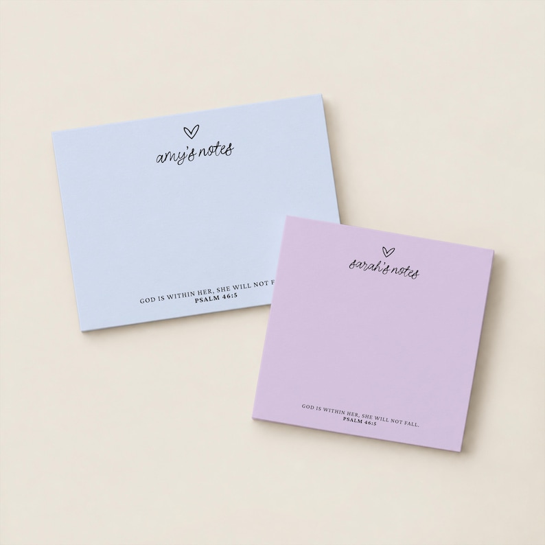 May include: Two rectangular paper notepads in light blue and light purple. The blue pad features the text 'amy's notes' with a heart icon and 'GOD IS WITHIN HER, SHE WILL NOT FALL. PSALM 46:5'. The purple pad says 'sarah's notes' with a heart.