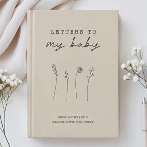 Op de afbeelding: Beigekleurig notitieboek met de tekst "Letters to my baby" en "From my heart (because you're still there)" in zwarte tekst. Het notitieboek heeft een eenvoudige lijntekening van vier bloemen.