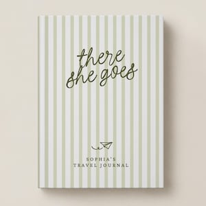 May include: A rectangular journal with a vertical striped pattern in white and sage green. The cover features the dark green cursive text there she goes, a small paper airplane icon, and the text SOPHIA'S TRAVEL JOURNAL in block letters.