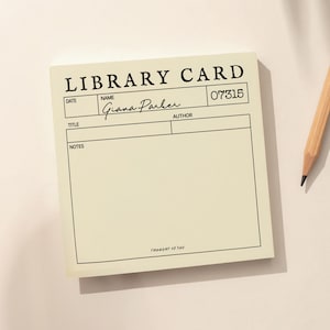 May include: A cream-colored library card notepad with black text and lines. The text "LIBRARY CARD" is at the top, with fields for date, name, title, author, and notes. The name "Giana Parker" is handwritten. A pencil rests on the side.