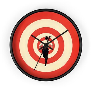 Puede incluir: Un reloj blanco y negro con un diseño de diana rojo y blanco. Una persona con camisa blanca y pantalón negro corre hacia el centro de la diana.