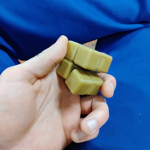 May include: A stack of four light green, cube-shaped objects. The cubes are held in a hand against a blue background. The objects appear to be made of a solid material.