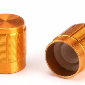 Puede incluir: Dos pomos de metal dorado con un diseño acanalado. Los pomos se utilizan para ajustar el volumen u otras configuraciones en dispositivos electrónicos.