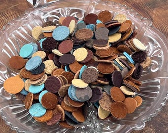 May include: A collection of small, circular leather pieces in various colors including brown, tan, blue, and black, piled inside a clear, pressed glass dish with a scalloped edge and two integrated handles on opposite sides.