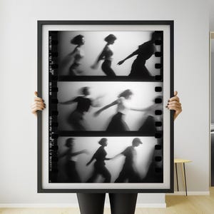 May include: Black and white framed print featuring three rows of blurred figures in motion, resembling a film strip. The figures are silhouetted against a bright background, creating a sense of movement and mystery. The frame is black.