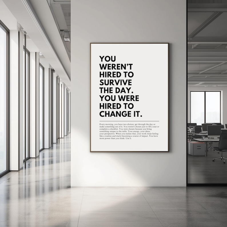 Puede incluir: Un p&oacute;ster enmarcado con el texto "YOU WEREN'T HIRED TO SURVIVE THE DAY. YOU WERE HIRED TO CHANGE IT." en un entorno de oficina moderno. El p&oacute;ster tiene un fondo blanco con texto negro.
