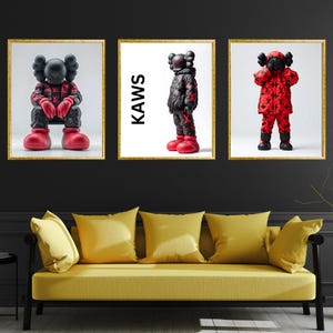 May include: Three framed art prints featuring black and red Kaws figures. The middle print has the word "KAWS" in white text.