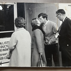 Foto vintage de la década de 1960: Pareja besándose frente a la oficina de reclutamiento de soldados alistados. Fotografía en blanco y negro montada sobre tabla de 33 x 25 cm.