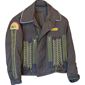 Puede incluir: Una chaqueta gris oscuro con cuello blanco y detalles de cremallera verde. La chaqueta tiene un parche en la manga izquierda con un arcoíris y un diseño de flor. La chaqueta tiene una cremallera y varios bolsillos.