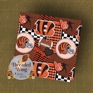May include: A digital embroidery design featuring a football theme with orange and black tiger-striped helmets, a heart-shaped football, a number one foam finger, and a football field grid pattern. The text Threaded Wing Digital Designs is visible.