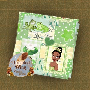 Könnte beinhalten: Gefalteter Stoff mit einem Patchwork-Design aus grünen, gelben und weißen Quadraten. Das Design enthält Bilder von Fröschen, einer Seerose und einer Prinzessin. Der Stoff trägt den Text "Threaded Wing Digital Designs" auf einem kreisförmigen Logo.