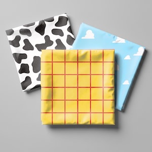 May include: Three folded fabric squares featuring distinct patterns: one with a black and white cow print, one with a light blue background and white cloud shapes, and one with a bright yellow background overlaid with a red grid pattern.