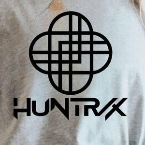 Può includere: Primo piano di una felpa grigio chiaro con un design geometrico nero e la scritta "HUNTR/X" in grassetto. Il design è un motivo stilizzato e interconnesso.
