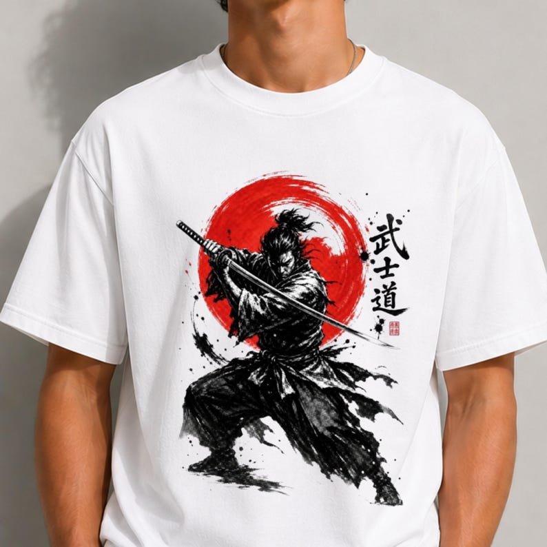 Op de afbeelding: Een wit T-shirt met korte mouwen en een zwarte inktillustratie van een samoerai die een katana vasthoudt. Achter de figuur bevindt zich een grote rode cirkel. Rechts van de samoerai staan zwarte Japanse karakters en een klein rood stempel.