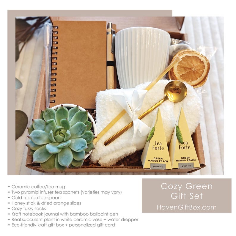 K&ouml;nnte beinhalten: Eine Geschenkbox gef&uuml;llt mit einer wei&szlig;en Keramiktasse, einer kleinen Sukkulentenpflanze, einem wei&szlig;en Handtuch, zwei Teebeuteln, einem goldenen L&ouml;ffel, einem Notizbuch und einem Stift. Die Box ist aus braunem Kraftpapier und hat ein wei&szlig;es Band darum gebunden. Der Text "Cozy Green Gift Set" und "HavenGiftBox.com" ist auf der Box aufgedruckt.