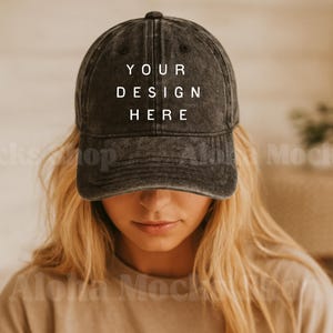 Könnte beinhalten: Dunkelgraue Baseballkappe mit dem Text "YOUR DESIGN HERE" in weißen Blockbuchstaben. Die Kappe wird von einer Person mit blonden Haaren getragen. Die Kappe hat einen gebogenen Schirm und einen Knopf oben.