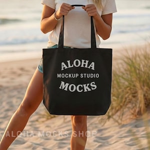 May include: Black tote bag with white text that reads "ALOHA MOCKUP STUDIO MOCKS". The bag is held by a person on a beach. The words "ALOHA MOCKS SHOP" are at the bottom of the image.