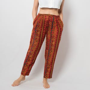 Peut inclure: Pantalon rouille avec un motif géométrique dans les tons de jaune, vert et bleu. Le pantalon a une taille haute et des poches. Le tissu semble léger, adapté aux températures plus chaudes. Fait partie d'une collection de vêtements vintage.