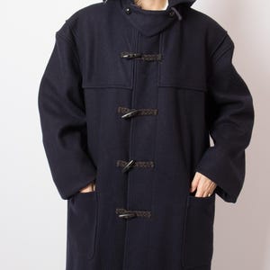 Puede incluir: Un abrigo tipo duffle coat azul marino con capucha y cierres de palanca. El abrigo tiene dos bolsillos delanteros y está hecho de un material grueso y cálido. Un estilo clásico, ideal para el frío, de unos 120 cm de largo.
