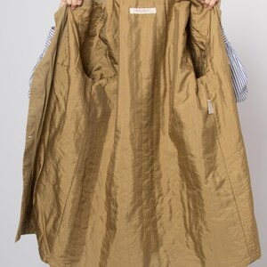 May include: A tan-colored jacket with a shiny, quilted gold-colored lining. The jacket is open, revealing the interior with two pockets and a label. The exterior of the jacket is a matte tan color.