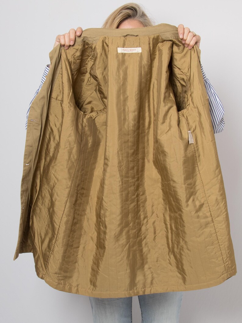 May include: A tan-colored jacket with a shiny, quilted gold-colored lining. The jacket is open, revealing the interior with two pockets and a label. The exterior of the jacket is a matte tan color.