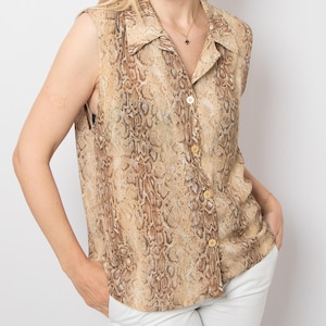 May include: A sleeveless button-down shirt featuring a tan and brown snakeskin print pattern. The shirt has a classic collar, a front button placket with four visible light-colored buttons, and a relaxed fit that falls at the hip level.