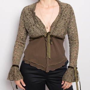 May include: A brown lace top with long sleeves and a V-neckline. The top features a dark green ribbon tie at the waist and dark green velvet trim on the cuffs. The top is paired with black pants.