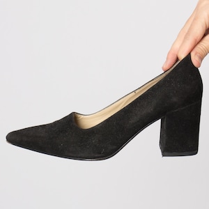 Può includere: Décolleté nere in camoscio con punta a punta e tacco largo. Il tacco è alto circa 7.6 cm. La scarpa ha un design classico e un colore neutro, adatta a vari outfit.