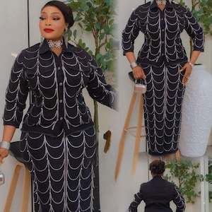 May include: Black denim skirt suit with white beaded accents. The jacket has a collared neckline and long sleeves. The skirt is a pencil style. The suit is worn with silver heels and jewelry.