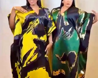 May include: Two women wearing flowing, V-neck dresses. One dress is yellow with black abstract patterns, the other is green with gold and black patterns. The dresses have wide sleeves and a loose fit, suitable for special occasions.