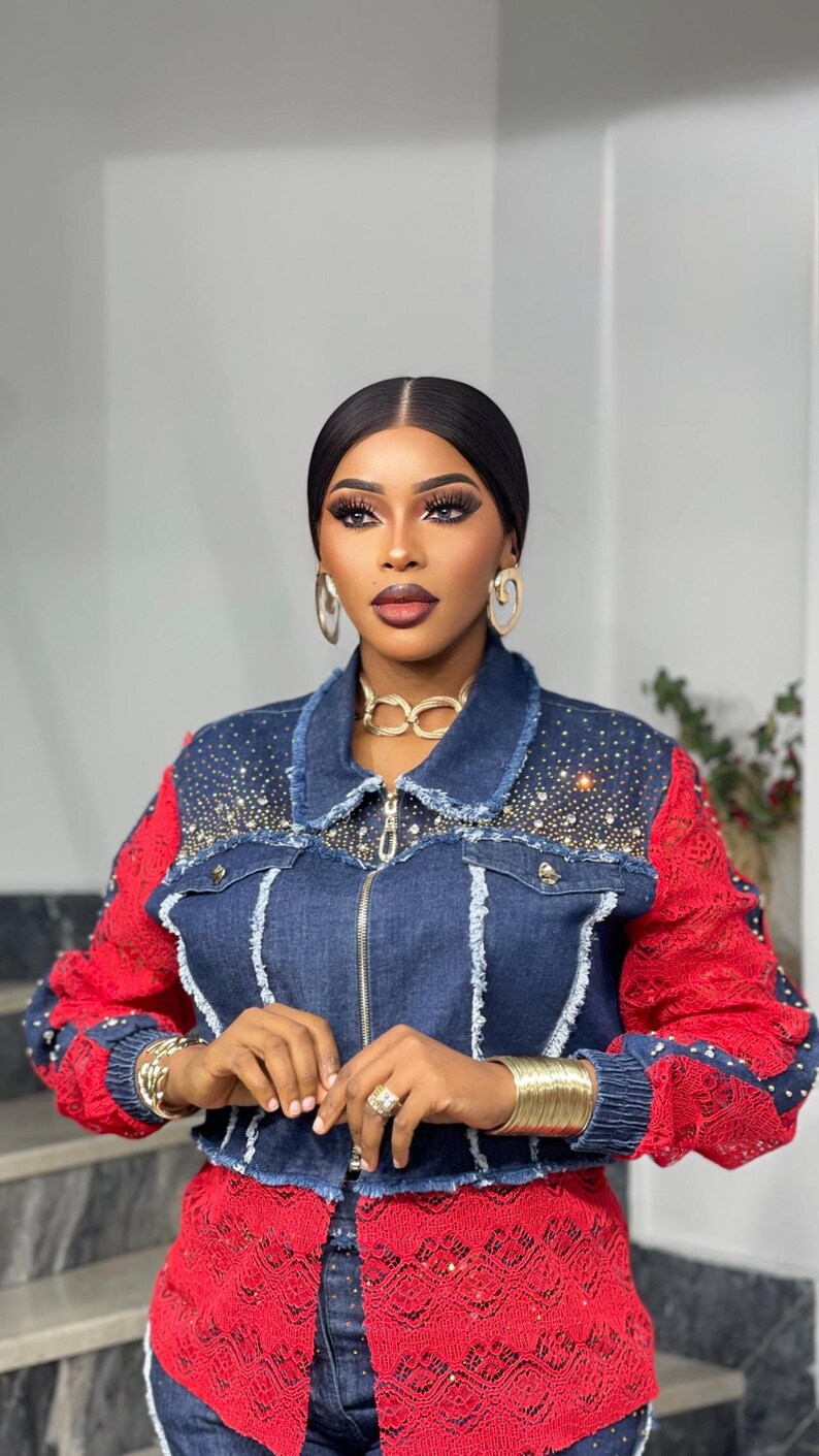 May include: A denim jacket with red lace sleeves and embellishments. The jacket features a zip-up front and is adorned with rhinestones. Gold jewelry, including a necklace, earrings, and bracelets, complements the outfit.