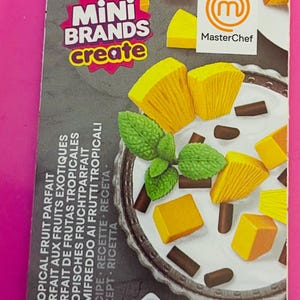 May include: A box for a Mini Brands Create set, featuring a tropical fruit parfait. The box includes the MasterChef logo and the text "Mini Brands Create". The parfait includes yellow fruit, chocolate, and mint.