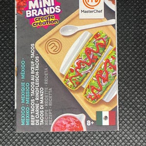 May include: A ZURU Mini Brands MasterChef box with miniature tacos. The box shows a wooden cutting board, a white spoon, and a small bowl of red sauce. The Mexican flag is present, and the box is marked "8+".