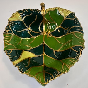 May include: A ceramic dish shaped like a large leaf with a glossy finish. The surface features a color palette of dark forest green, bright lime green, and yellow, with gold-painted veins and a gold-trimmed scalloped edge and stem.