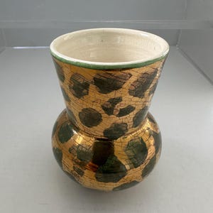 May include: A decorative vase with a bulbous base and a flared top. The vase features a gold and brown spotted pattern with a cracked glaze effect. The rim is trimmed with green.