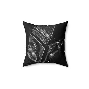 May include: Black and white photo of a vintage Yashika LM camera on a black pillow. The camera has two lenses and the text "Yashika LM" is visible on the side.