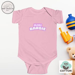 May include: Pink baby onesie with short sleeves and a snap closure. The onesie has the text "mini Barbie" in a purple and white font.