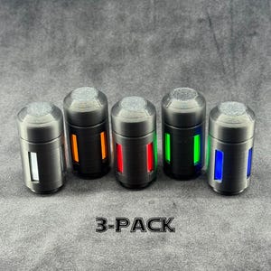 Puede incluir: Cinco objetos cilíndricos con acabado metálico y parte superior texturizada. Cada uno tiene una luz rectangular vertical de diferente color: blanco, naranja, rojo, verde y azul. El texto "3-PACK" está en la parte inferior.