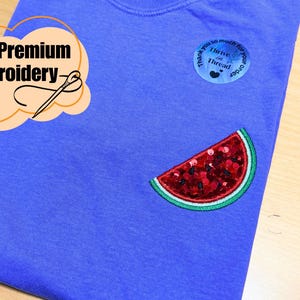 May include: A blue t-shirt featuring a watermelon slice sequin patch. The shirt has a small round patch with the text "Thank you so much for your order" and "Thrive in Thread". It also has a "Premium Embroidery" graphic.
