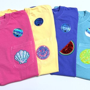 May include: Four short-sleeved t-shirts in pink, yellow, purple, and light blue, each featuring a chest pocket with a unique patch: a seashell, a smiley face, a watermelon slice, and a citrus slice. Each shirt includes a circular holographic sticker.
