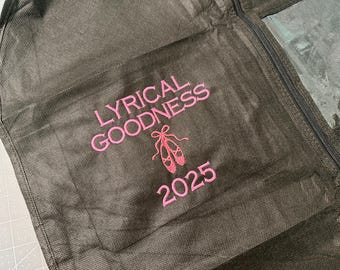 May include: A dark brown garment bag featuring pink embroidery. The embroidery reads "LYRICAL GOODNESS" above a ballet shoe design and the number "2025". The bag has a zip closure and a clear panel.