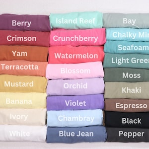 May include: A collection of folded t-shirts in various colors, including Berry, Crimson, and Yam. Each shirt displays a different color name in white text. Other colors include Island Reef, Chalky Mint, and Black.