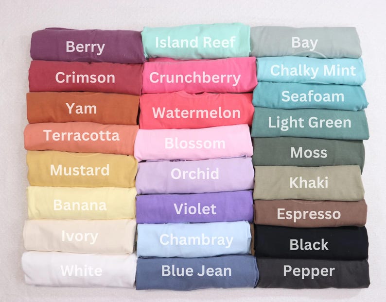 May include: A collection of folded t-shirts in various colors, including Berry, Crimson, and Yam. Each shirt displays a different color name in white text. Other colors include Island Reef, Chalky Mint, and Black.