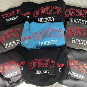 Puede incluir: Una colecci&oacute;n de sudaderas con tem&aacute;tica de hockey en varios colores, incluyendo negro, gris y azul claro. Cada sudadera presenta la palabra "KNIGHTS" en letras rojas arqueadas sobre "HOCKEY" en blanco. Algunas sudaderas tienen nombres y n&uacute;meros de jugadores.