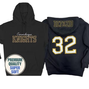 May include: Black hoodie with "Canandaigua KNIGHTS" in gold lettering. The front features a pocket and a circular graphic with "PREMIUM QUALITY SUPER SOFT". The back of a navy blue hoodie displays "DEFAZIO" and the number "32" in gold.