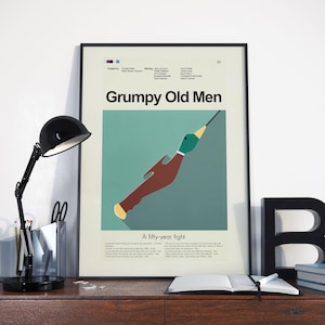 Op de afbeelding: Een ingelijste poster voor de film "Grumpy Old Men" met een gestileerde eendenillustratie. De poster heeft een turquoise achtergrond en de titel in het wit. Een zwarte bureaulamp en kantoorbenodigdheden staan op de voorgrond.