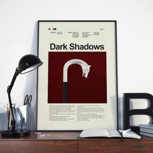 May include: Framed "Dark Shadows" poster featuring a stylized cane with a horse head handle against a burgundy background. The poster includes the show's title and credits. A black desk lamp and open book are in the foreground.