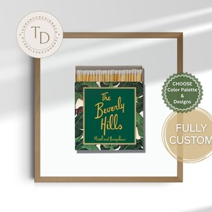 Peut inclure: Une boîte d'allumettes avec un motif de feuilles tropicales vertes et blanches. Le texte "The Beverly Hills Hotel and Bungalows" est en lettres dorées. L'ensemble est présenté dans un cadre en bois.