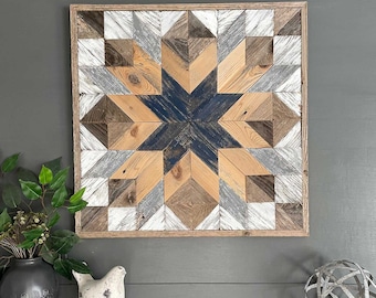 May include: A wooden wall art piece with a starburst design in shades of brown, gray, and blue. The starburst is made of individual wood pieces that are arranged in a geometric pattern. The piece is framed in a natural wood frame.