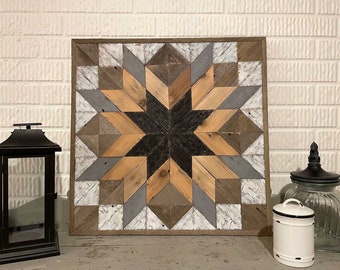 Puede incluir: Un tapiz de pared de madera con un diseño de estrella en forma de estallido en tonos marrones, grises y blancos. La estrella en forma de estallido está hecha de piezas individuales de madera que están dispuestas en un patrón geométrico. El tapiz de pared está enmarcado en un marco de madera marrón oscuro.